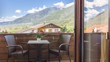 A balcony with wicker chairs, a table, and a potted plant.