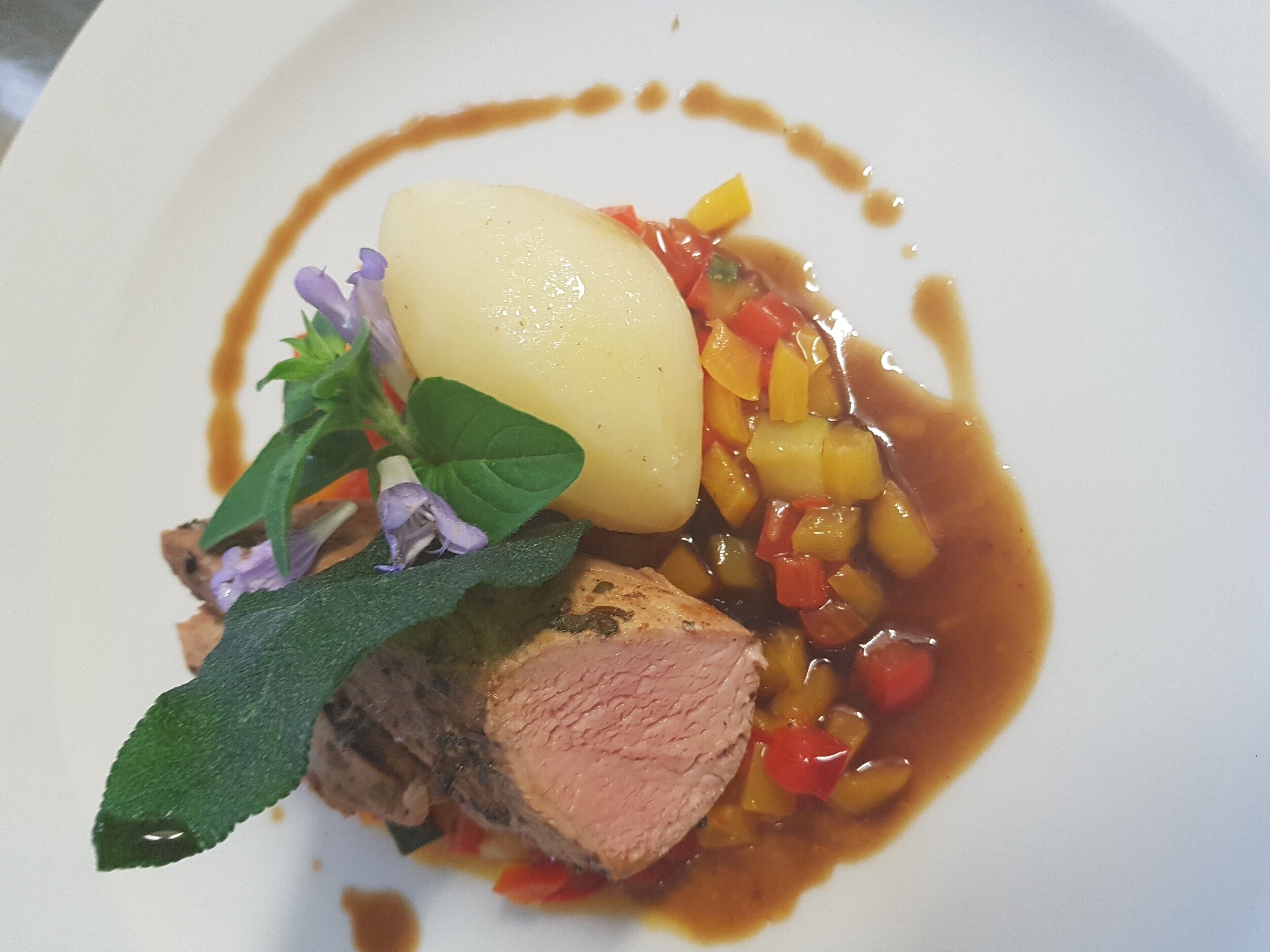 Ein Teller mit Fleischscheibe, gekochter Kartoffel und Gemüse in Soße.