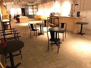 An indoor space with multiple tables and chairs, a wooden counter, and a visible door in the background.