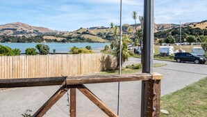 Vista de un lago con colinas al fondo, una valla de madera y una carretera con coches estacionados.