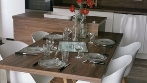 Une table à manger dressée avec de la vaisselle et des verres, entourée de chaises blanches, dans une cuisine moderne.