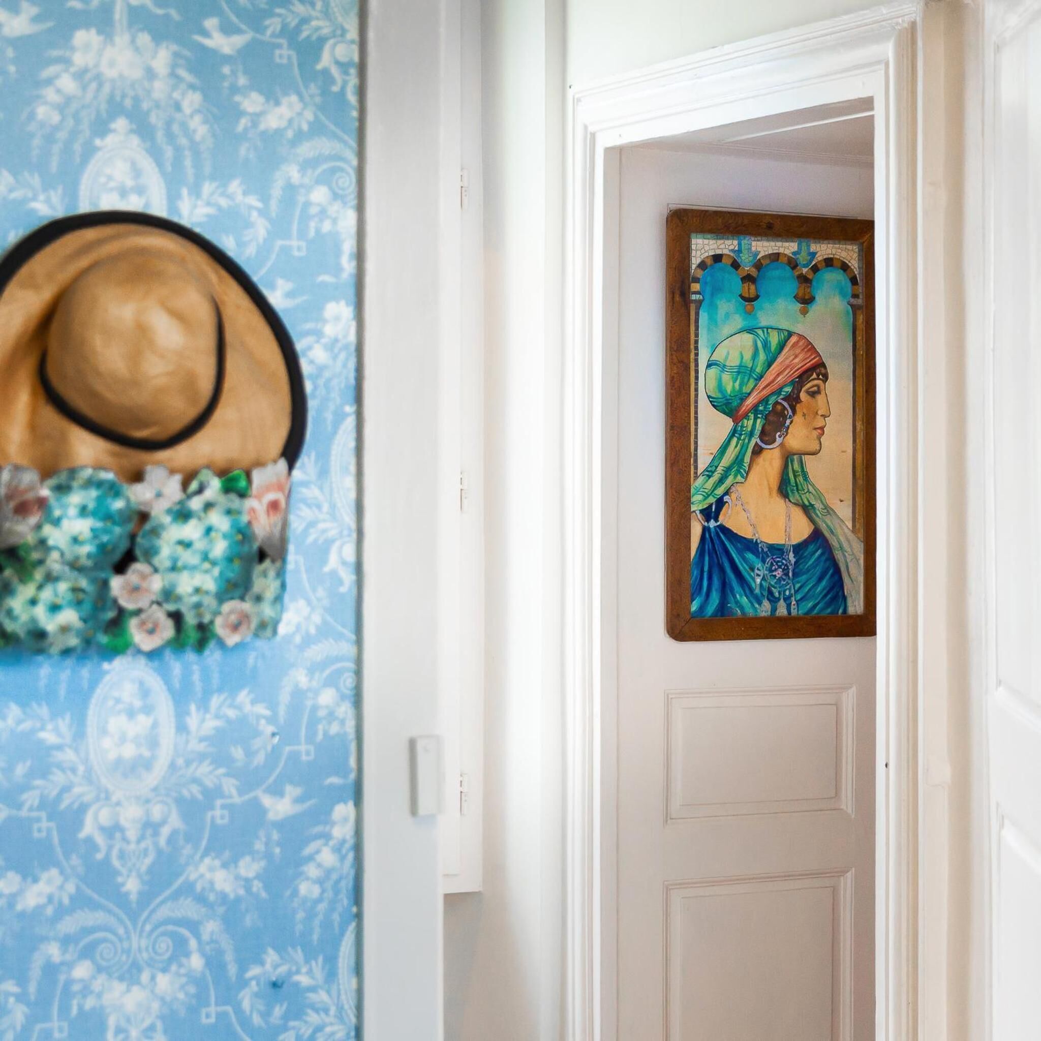 A hallway with a blue patterned wallpaper, a hat, and a framed artwork on the wall.
