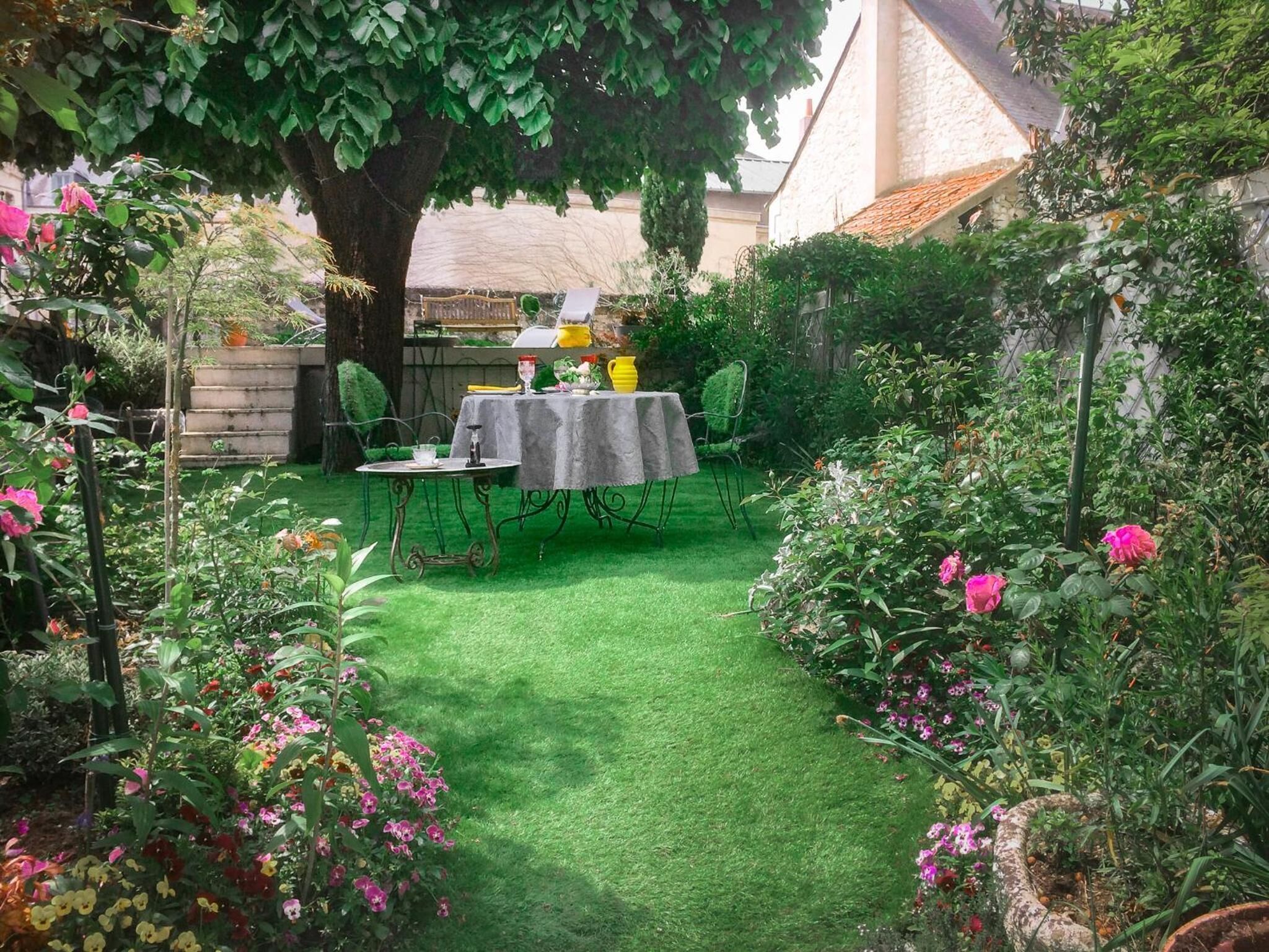 Een tuin met een tafel en stoelen onder een boom, omringd door diverse planten en bloemen.