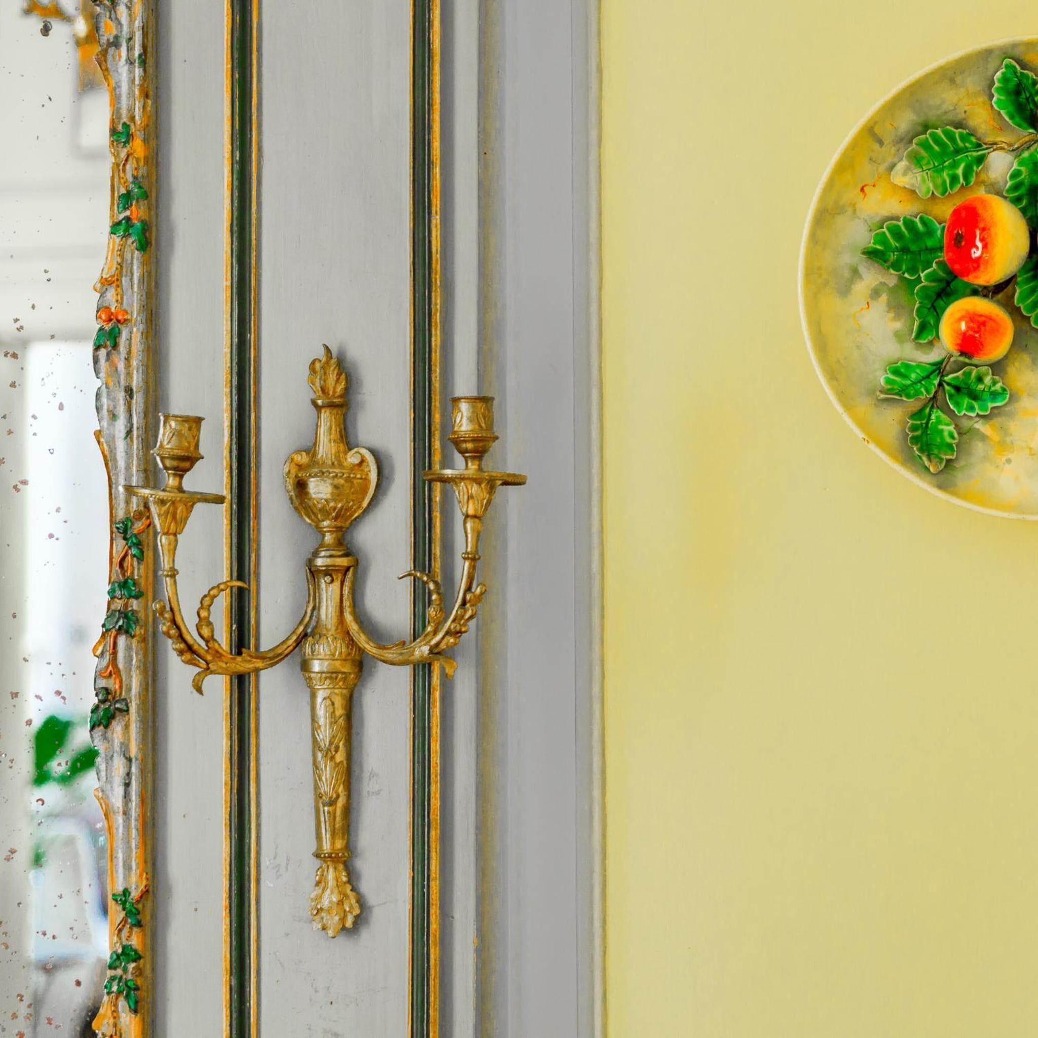 Una habitación con un candelabro decorativo y un arreglo de frutas en la pared.