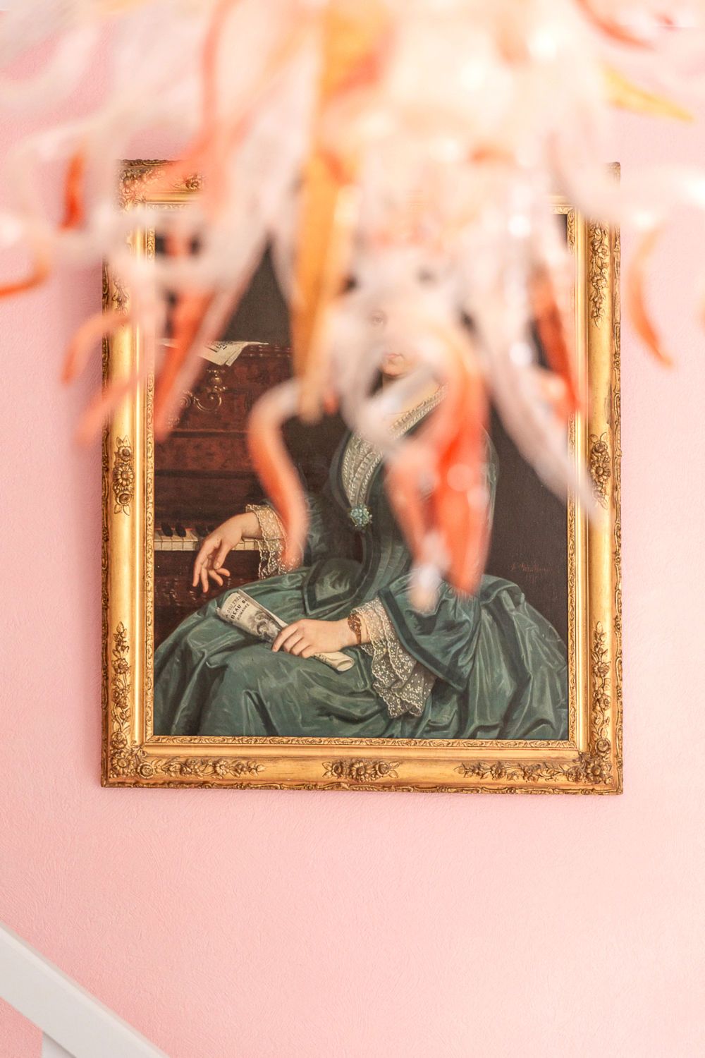 A framed portrait of a person in a green dress with gold detailing, set against a pink wall.