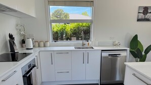 A modern kitchen with white cabinets, a dishwasher, a stove, and a window with a view of greenery.