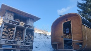 Een houten blokhut met een sauna en een houtopslag, omgeven door sneeuw.