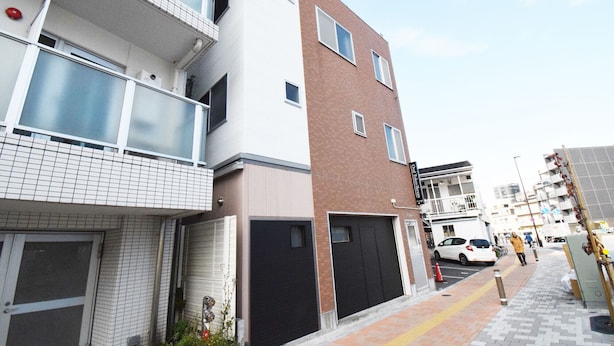 A multi-story residential building with a mix of brick and white exterior walls, a visible garage door, and a pedestrian pathway. - Oval Tokyo Ikesan 201 (Tokyo)