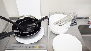 A kitchen with a stove, a frying pan, a spatula, a stack of white plates, and a set of glasses. - Oval Tokyo Ikesan 201 (Tokyo)