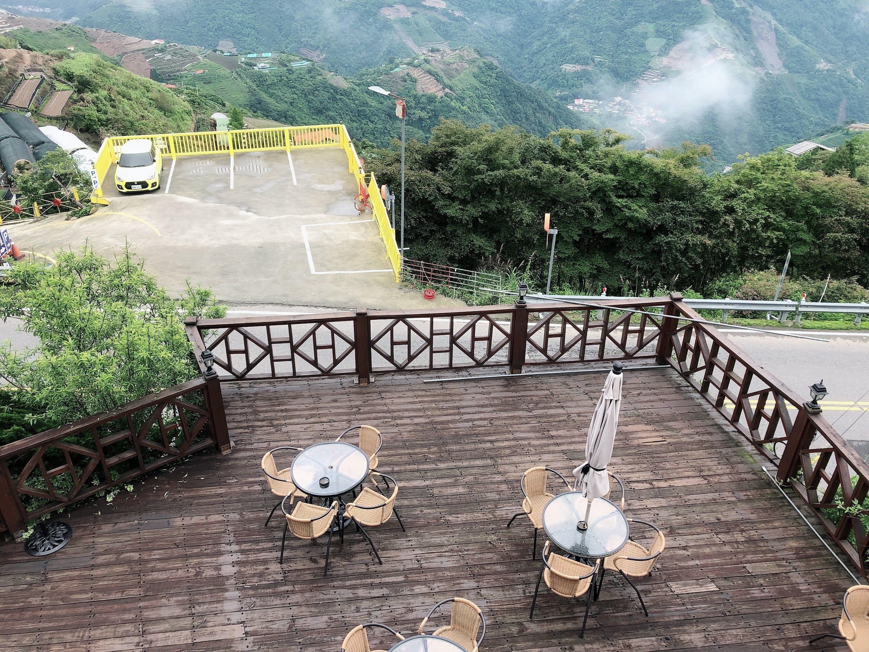 Una terraza de madera con mesas y sillas, con vistas a un estacionamiento y un valle verde.