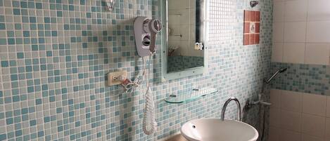Un baño con pared de azulejos, un lavabo, un espejo, un perchero para toallas y una zona de ducha.
