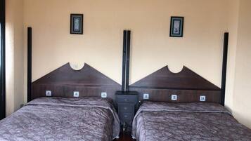 A double room with two beds, each with a wooden headboard and a floral-patterned bedspread. There are two small framed pictures on the wall above each bed.