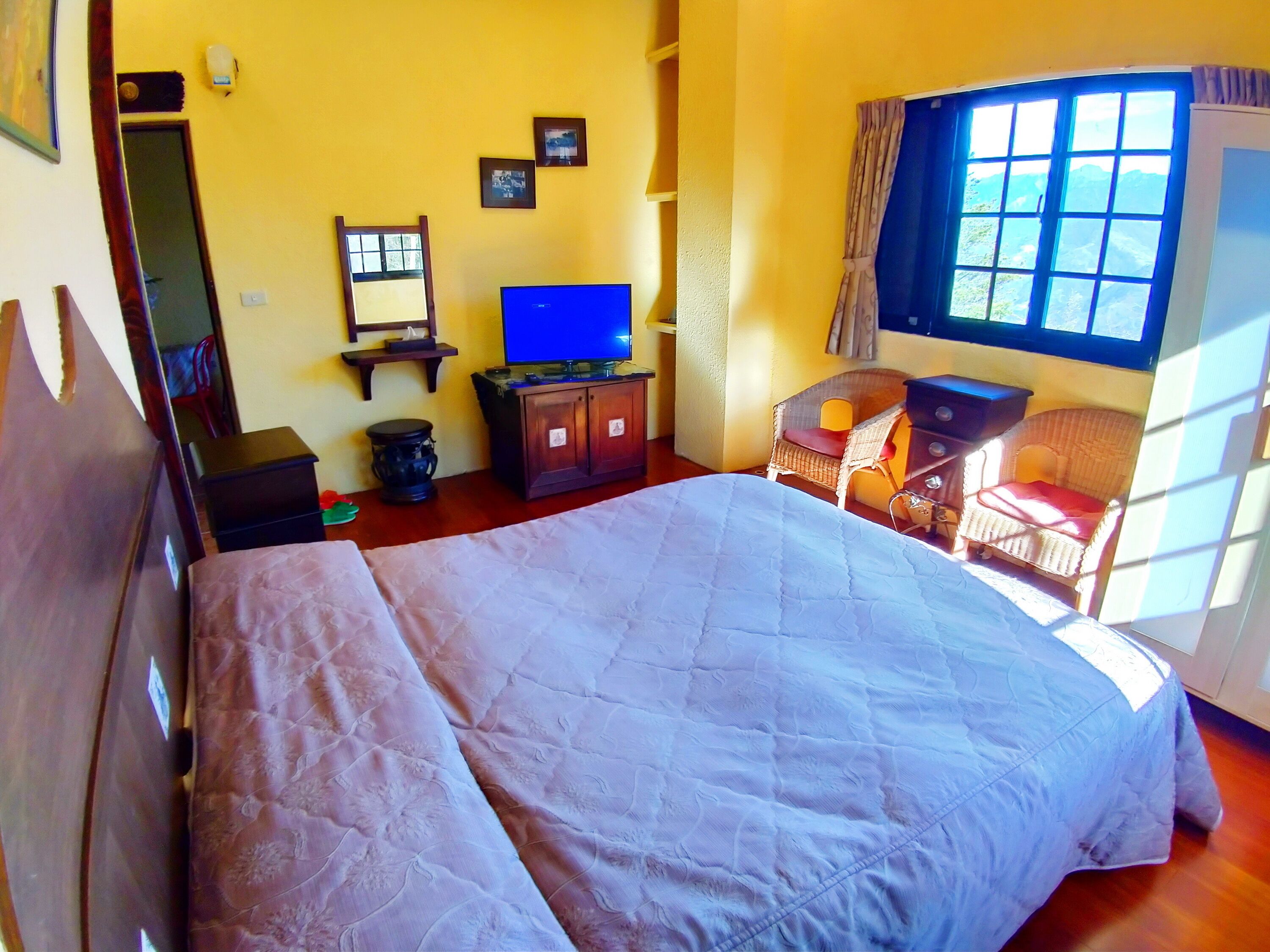 A bedroom with a bed, a television, a small table, a chair, and a window with a view of the outdoors.