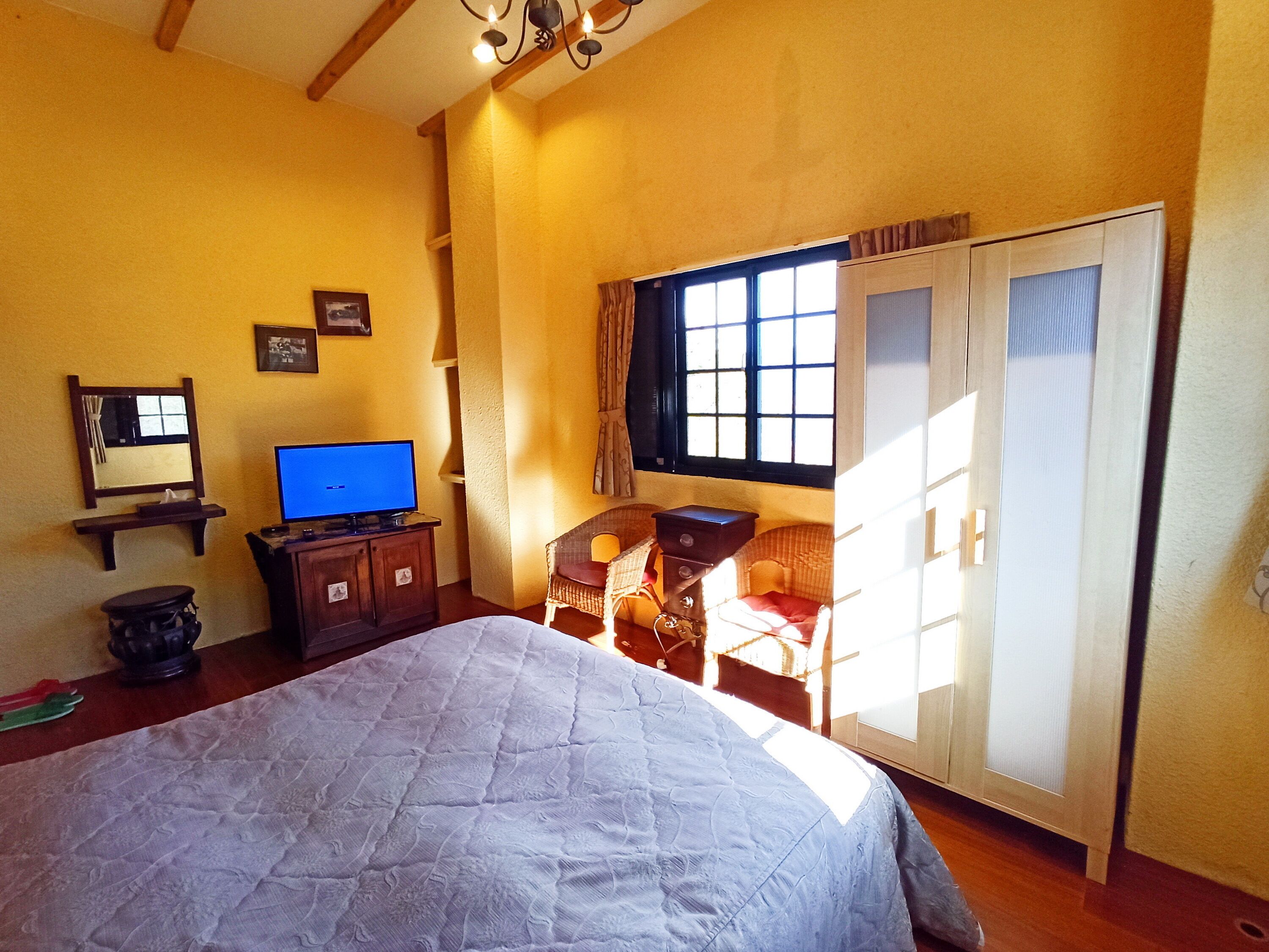 A bedroom with a bed, a desk with a computer, a wardrobe, and a window with curtains.