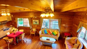 A cozy wooden cabin interior with a dining area, a sofa with colorful cushions, and a kitchen with wooden cabinets. - Nuowei Senlin Cottage (Ren'ai)