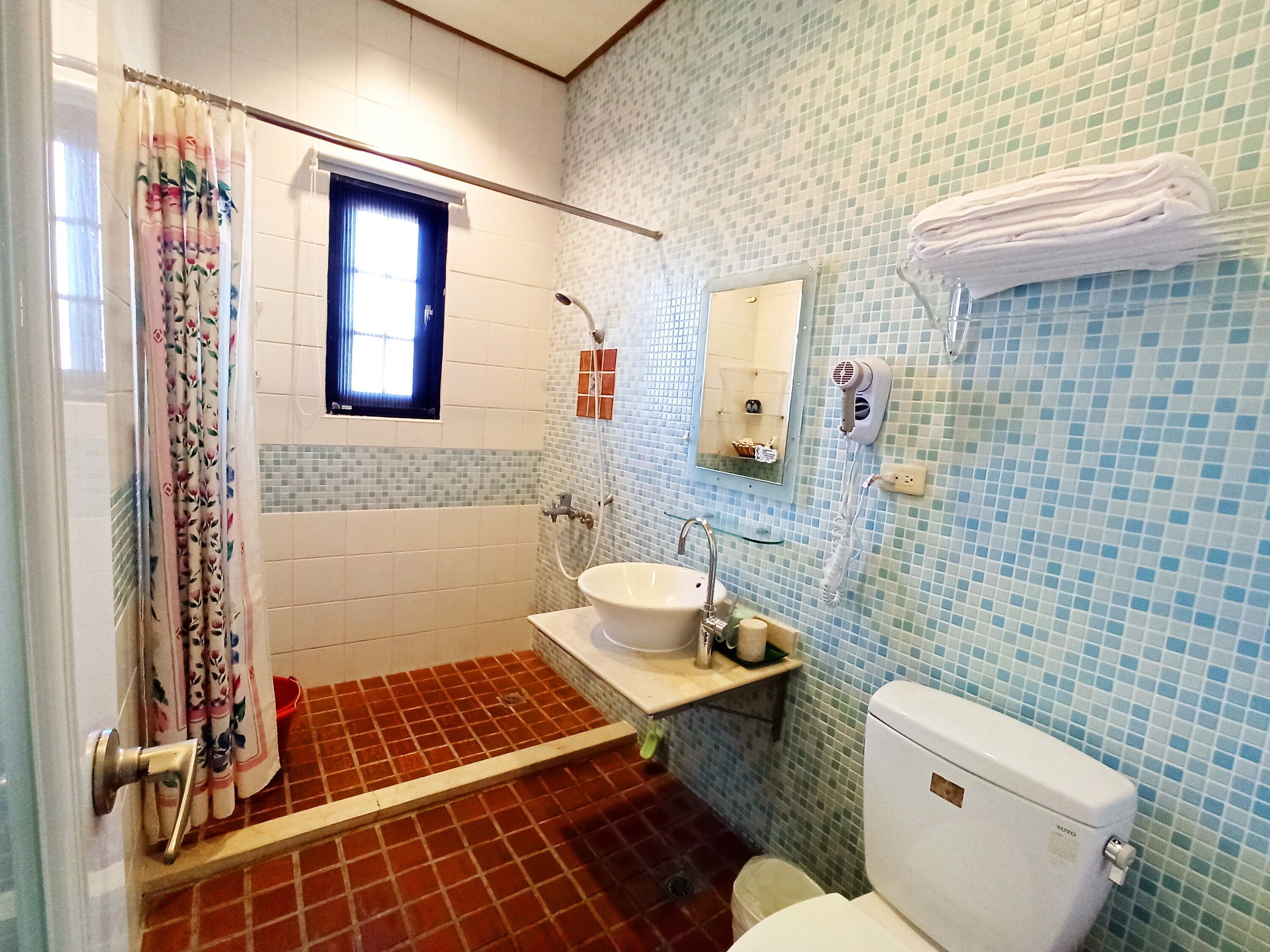 Een badkamer met douche, wastafel, toilet en een klein raam.