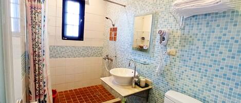 Een badkamer met douche, wastafel, toilet en een klein raam.