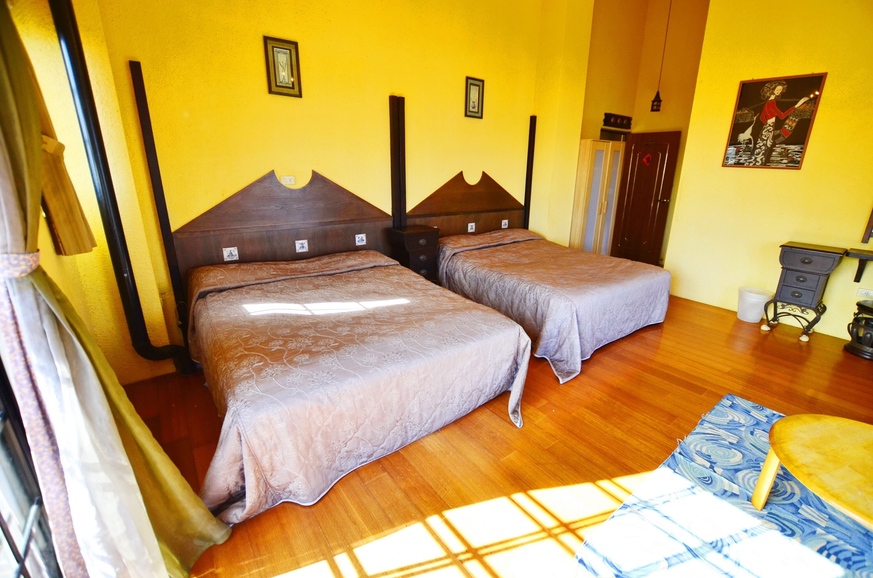 A room with two beds, wooden flooring, a small table, and a chair.
