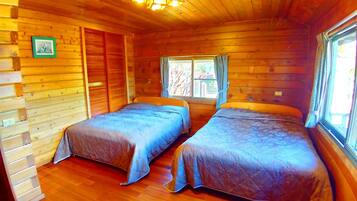 A cabin with two beds, wooden walls, a window with curtains, and a wooden ceiling with a light fixture.