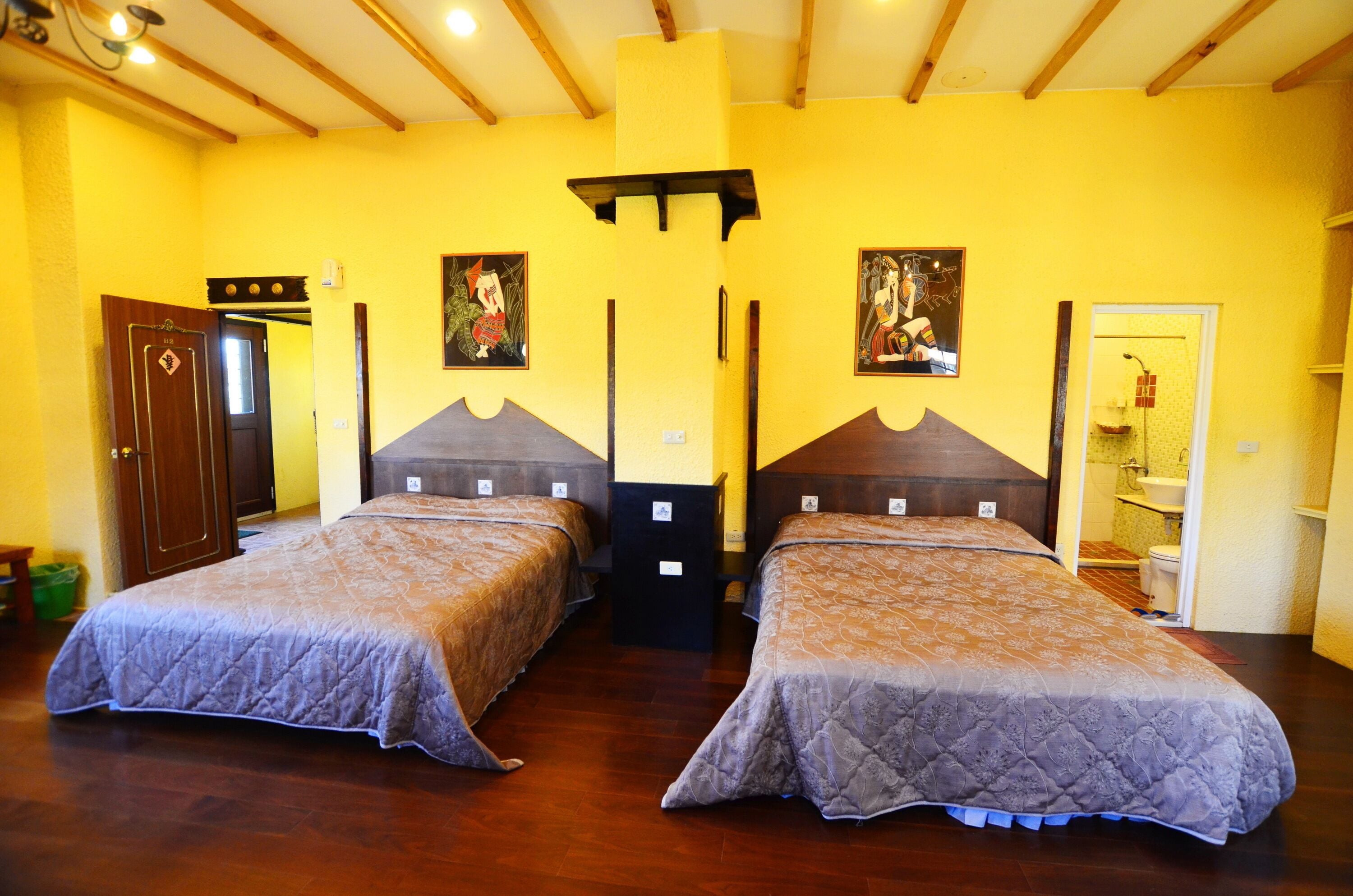 A room with two beds, wooden flooring, yellow walls, and a wooden ceiling.