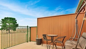 Une terrasse en bois avec une chaise suspendue, une petite table et une chaise en osier.