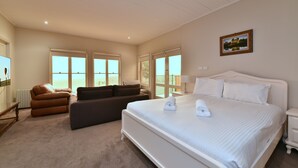Une chambre d’hôtel avec un grand lit, un canapé, un bureau et une vue sur la mer par les fenêtres.