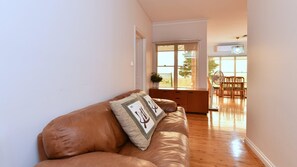 A living room with a brown leather sofa, a wooden cabinet, and a dining area with a table and chairs.