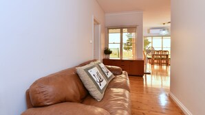 Uma sala de estar com sofá de couro marrom, janela com vista e área de jantar com mobiliário de madeira.
