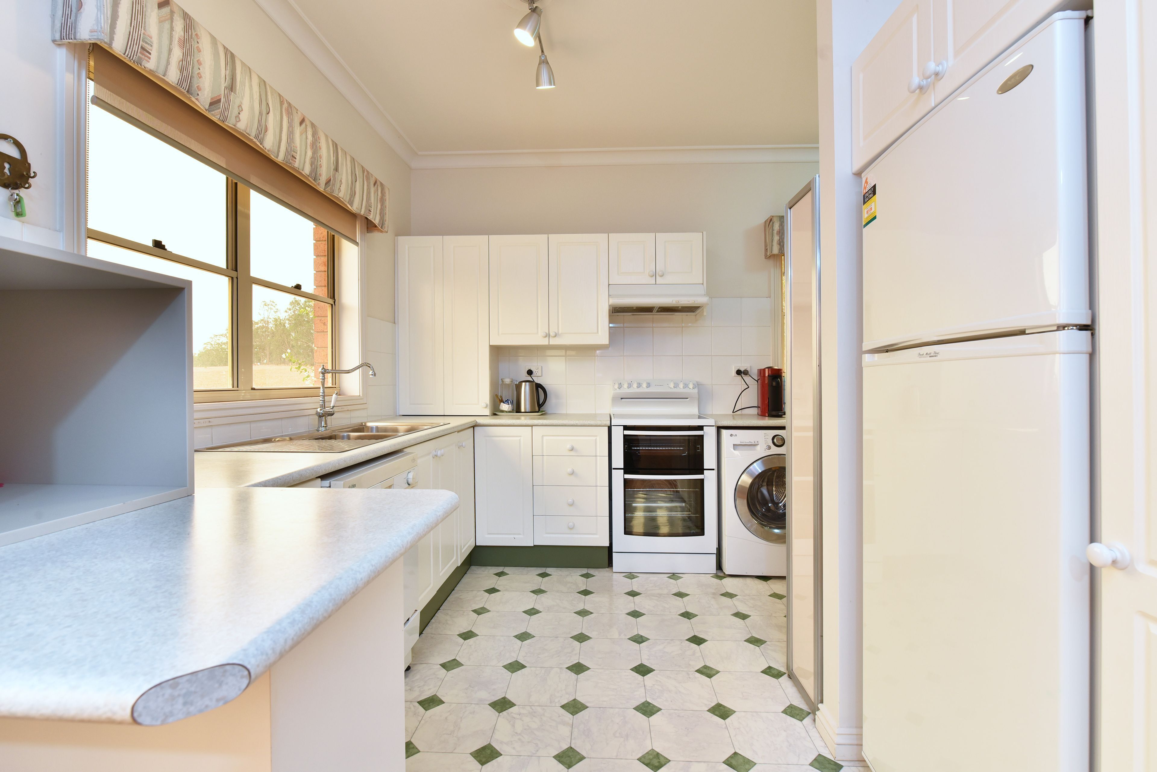Une cuisine avec des meubles blancs, un évier, une cuisinière, un four et un lave-linge.