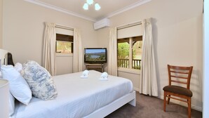 Quarto de hotel com cama, televisão, cadeira e janelas com cortinas.