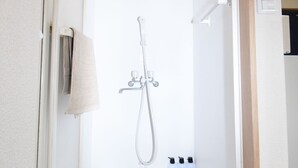 Ein kleiner, geschlossener Duschbereich mit Handbrause, einer Wandleuchte und einem Handtuch an der Tür.