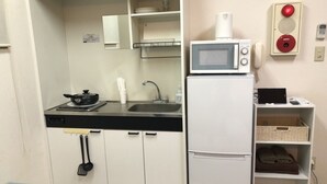 Eine kleine Küchenzeile mit Mikrowelle, Spüle und Herd. Es gibt Schränke, einen kleinen Kühlschrank und ein Regal mit Korb und Handtüchern.