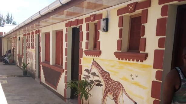 A building with a giraffe mural, red and beige walls, and potted plants. - Adonai Guest House (Mtwapa)