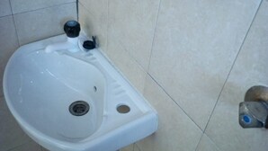 A bathroom with a white pedestal sink, a wall-mounted faucet, and a floor-mounted faucet. - Adonai Guest House (Mtwapa)