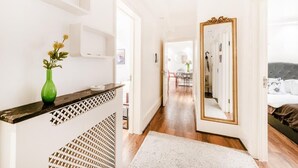 A hallway with a wooden floor, a white wall, and a mirror with a gold frame. - My Lady (London)