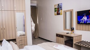 Een hotelkamer met een bed, een kledingkast, een kaptafel met spiegel, een televisie en een schilderij aan de muur.