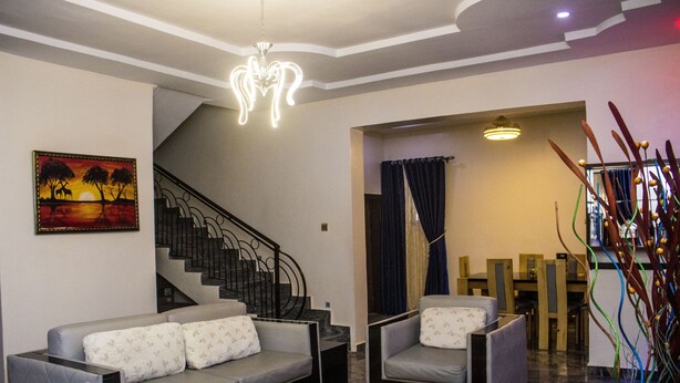 Een woonkamer met een bank, fauteuils, een trap en een eethoek.