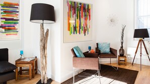 Una sala moderna con suelo de madera, un sofá negro, una mesa de centro de madera, una lámpara de pie y arte abstracto en las paredes.