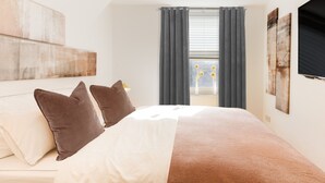 Un dormitorio moderno con una cama grande, cortinas oscuras y un televisor montado en la pared.