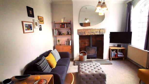 A living room with a sofa, ottoman, TV, fireplace, bookshelf, and a mirror. - Heritage Millworkers Cosy Cottage (Shipley)