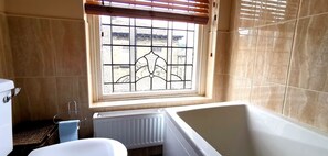 Ein Badezimmer mit Badewanne, einem Fenster mit dekorativem Gitter, einem Heizkörper und einer Toilette.