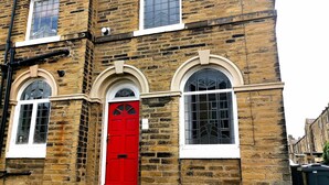 A brick building with three arched windows and a red door. - Heritage Millworkers Cosy Cottage (Shipley)