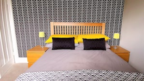 A bedroom with a bed, two bedside tables, and a patterned wall. - Heritage Millworkers Cosy Cottage (Shipley)