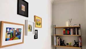 A room with a bookshelf, framed artworks, and a small decorative item on the shelf. - Heritage Millworkers Cosy Cottage (Shipley)