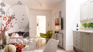 Une cuisine moderne avec une table à manger en verre, une chaise verte et un fauteuil blanc. On y trouve un îlot de cuisine avec un évier et un plan de travail sur lequel sont posées des bouteilles et une plante.