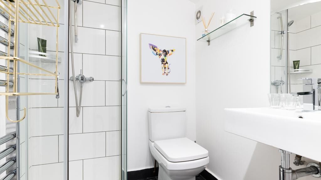 Une salle de bain moderne avec une douche à parois de verre, des toilettes blanches et un lavabo blanc surmonté d’une étagère en verre.