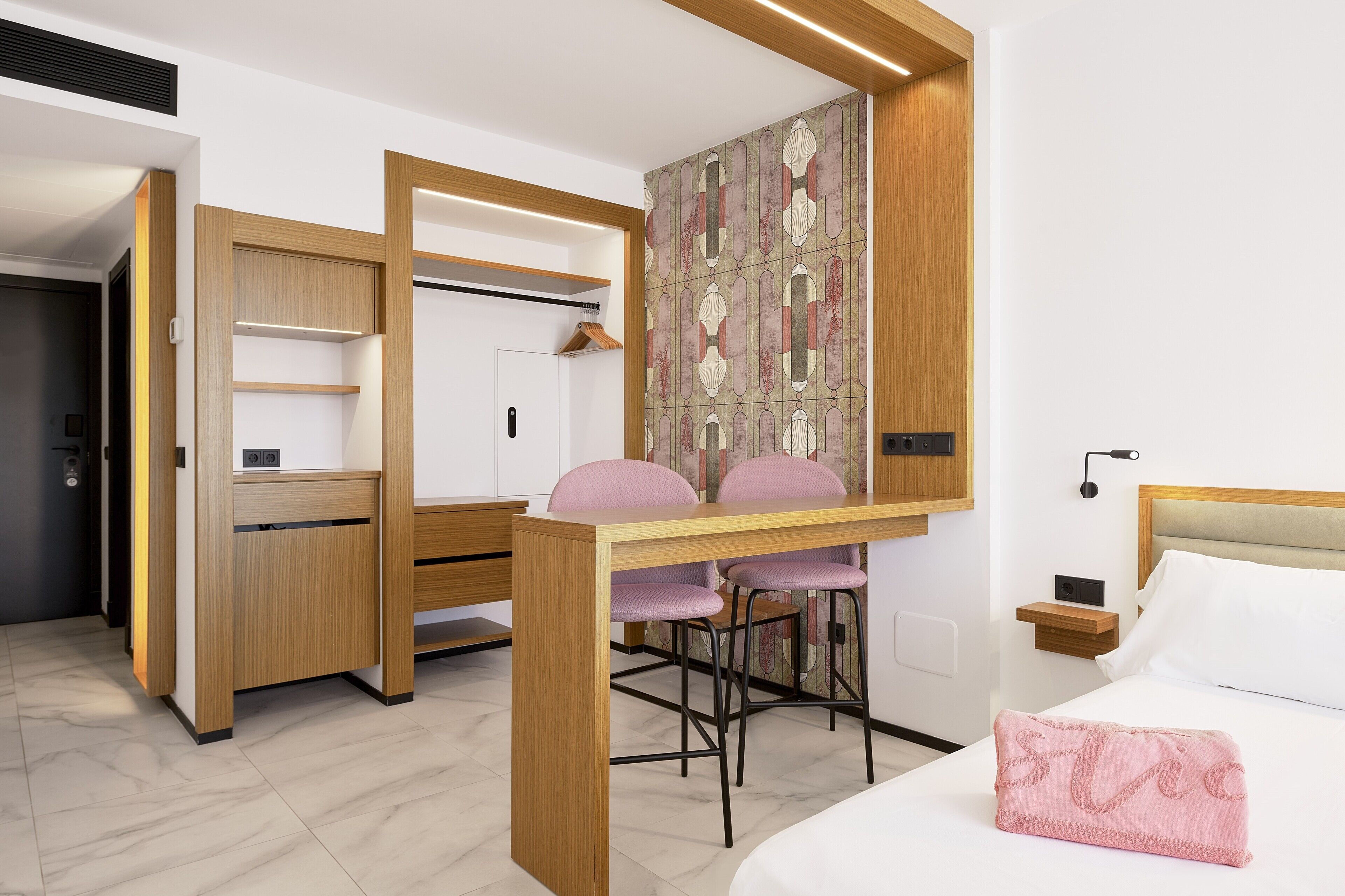 A modern bedroom with a bed, a desk with two chairs, a wardrobe, and a nightstand.