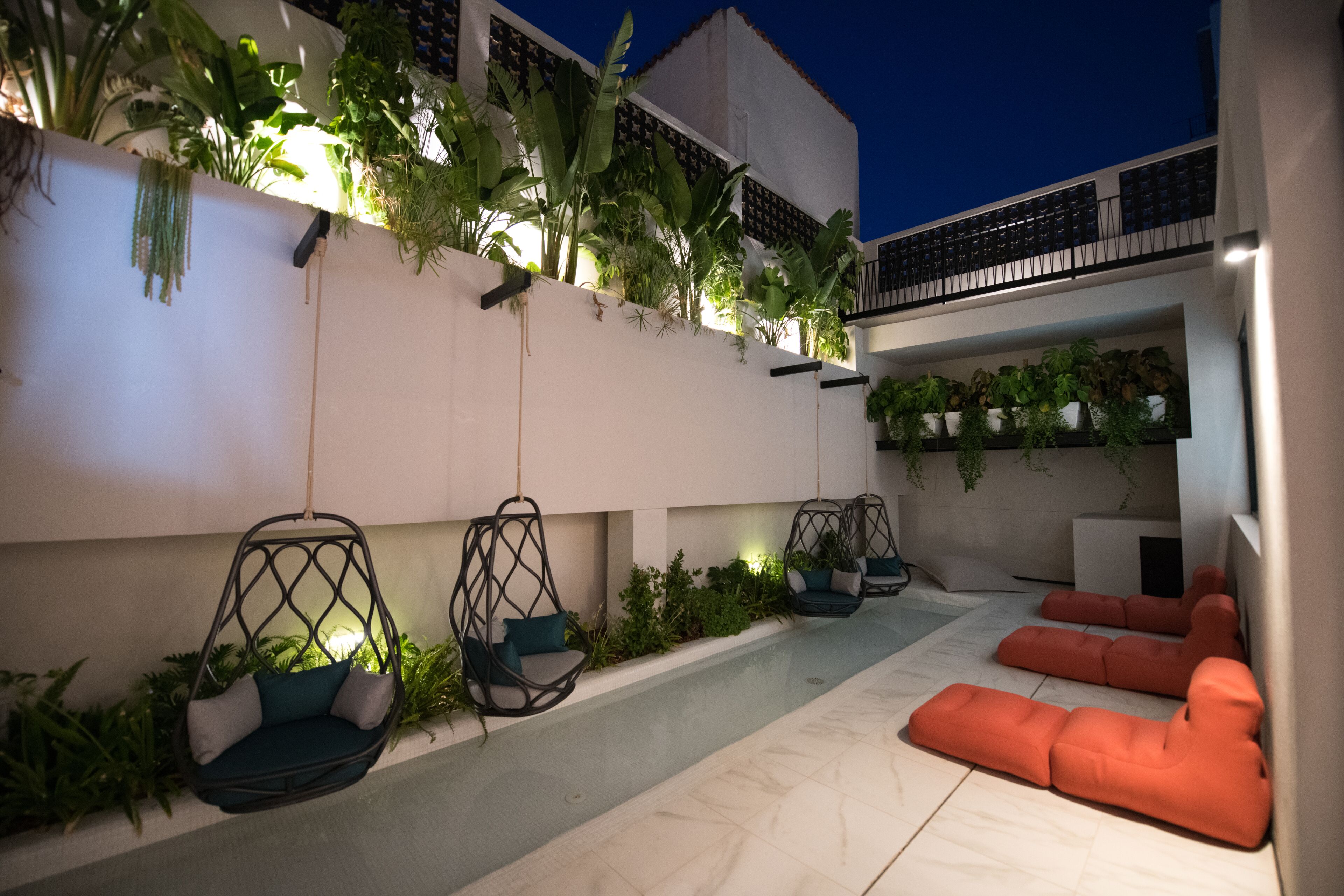 Un espace extérieur moderne aménagé avec des fauteuils suspendus et un canapé, le tout entouré d’une végétation luxuriante et de plantes.