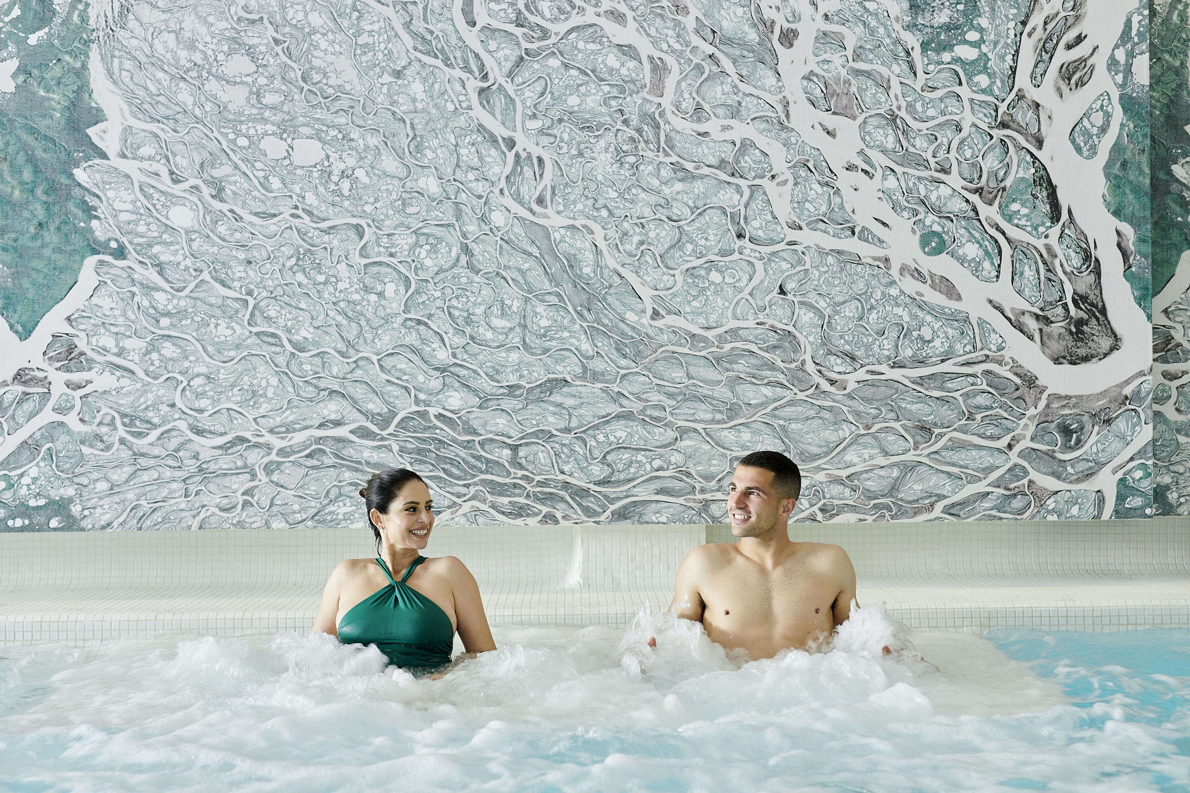 Een koppel in een jacuzzi, met een marmeren muur op de achtergrond.