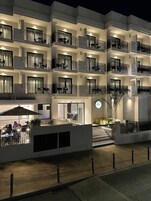 Un hotel moderno con varios balcones, mobiliario exterior y una entrada bien iluminada.